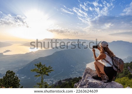 A happy girl with a backpack photographs the seascapes of Montenegro from the top of the mountain