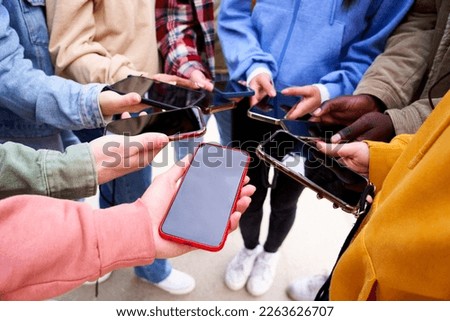 Large group of young teenagers with cell phones standing in circle. People showing their mobiles to camera with dark screen. Concept of addiction and social networking. Close up.