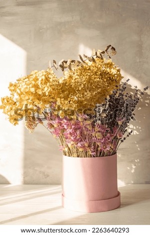  Bouquet of delicate dried hydrangea flowers and a lavender and lilac dried flowers in a  pink hat box on a gray background. Light calm photo.