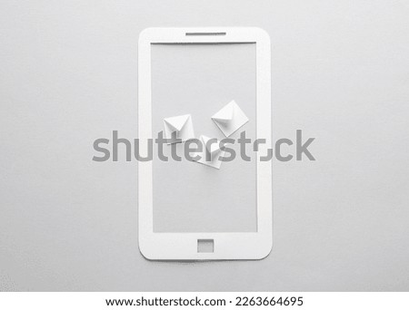 Paper-cut smartphone with envelopes on gray background.