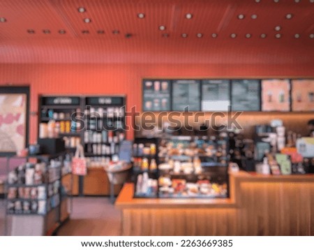 Blurred picture of cashier counter of a coffee shop with menu list on board hanging on the wall behind the counter and shelves for displaying merchandise in relaxing atmosphere. 