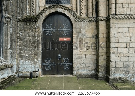 Large wooden doors seen at the entrance to a crypt within a famous English cathedral. A sign gives notice on another entrance for the public.