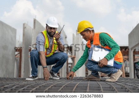 Foreman and laborer checking steel reinforcement cage for making precast concrete wall in construction site. Workers wearing vest and helmet safety working construction site.