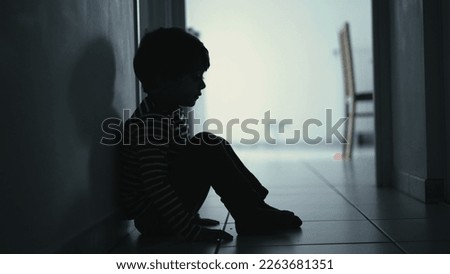 Sad child suffering from depression sitting alone in corridor feeling loneliness. Scared fearful small boy covering face in silhouette at home Royalty-Free Stock Photo #2263681351