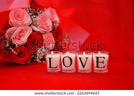 Candles kept against a red background with pink and red roses used as a prop at the back.