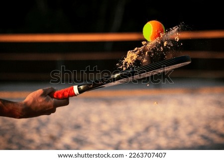 Beach tennis racket and ball. Man holding racket with sand and beach tennis ball on court. Royalty-Free Stock Photo #2263707407