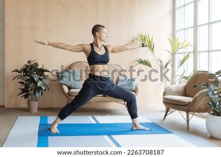 short haired athletic woman standing in yoga warrior pose in home loft interior Royalty-Free Stock Photo #2263708187