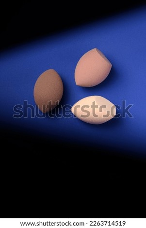 Three different cosmetic blenders on a blue background with a contrast shadow. Brown makeup sponges with pointed cutouts. Place for text. creative promotional photo for makeup artists. 