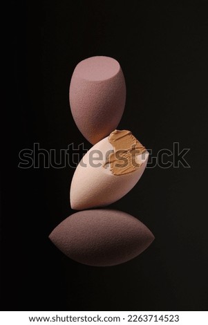 Three different beauty blenders on a black background with foundation.Brown makeup sponges with pointed cutouts. Makeup products. Beauty concept. Place for text. Creative advertising photo. Levitation