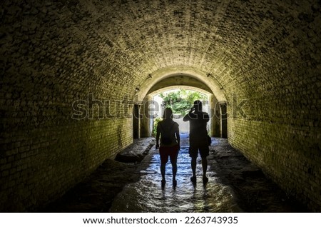 Silhouette of a couple, a man and woman, walking through dark arch. Stone castle wall of an Old Town.