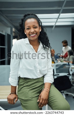 Vertical portrait of smiling young African American professional female sitting at modern office desk. Happy mixed race business woman team leader posing for photo at corporate meeting. 