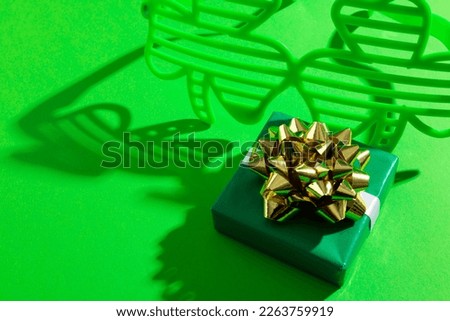 Image of green clover glasses with green present and copy space on green background. St patrick's day, irish tradition and celebration concept.
