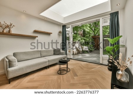 a living room with wood flooring and skylight above the couch is in front of an open glass door Royalty-Free Stock Photo #2263776377