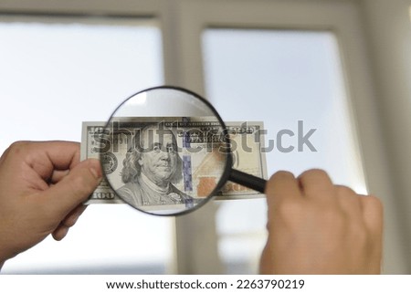 Checking counterfeit money light. 100 dollars against the window in his hand. Check for watermark on new hundred dollar bill. translucence of the American currency.