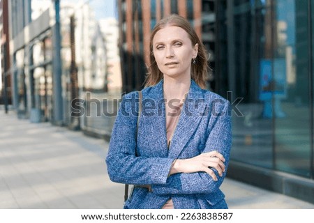 Happy business woman with professional appearance smiling confidently in city, in business clothes with crossed arms against the backdrop of an office building