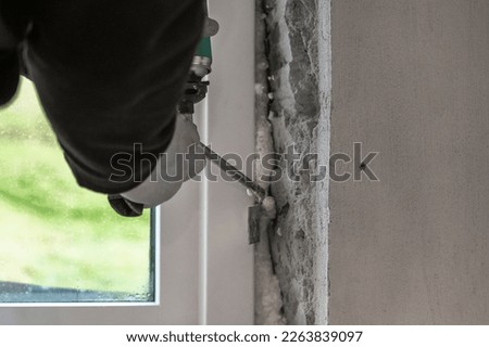 A man foaming a newly installed window in a window hole made in a concrete house wall. The foam helps to seal any gaps and improve insulation.