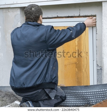 In this picture, a man is installing a window in a window hole. He is carefully fitting the window frame into the opening and securing it in place.