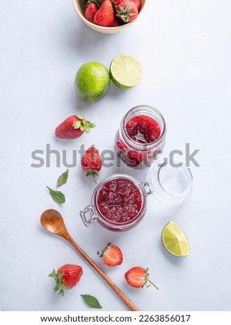 Homemade strawberry jam. Preserved food in a glass jar with fresh organic berries on a light background with lime. Eco-friendly farm products. Top view and copy space.
