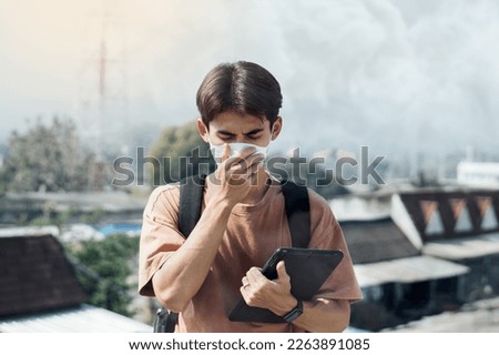 Portrait Asian young man wear N95 mask to protect PM 2.5 dust and air pollution. Young man wearing protection mask over smog city building with bad weather, pm2.5,City air pollution concept. Royalty-Free Stock Photo #2263891085