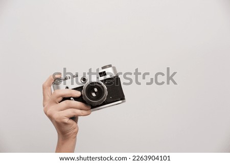 The raised hand of the photographer holds a retro camera