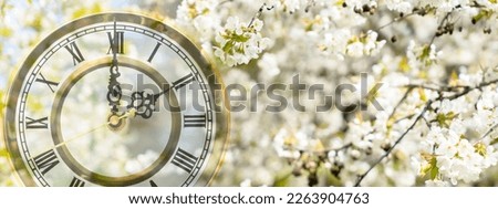 change to summertime clock in white flowering tree branches in spring,  watch face on blurred springtime nature background banner concept with double exposure