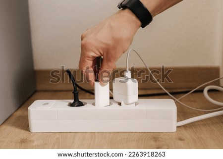 Human hand puts the charger into a filled extension cord. White cable connector. Close-up. Home routine Royalty-Free Stock Photo #2263918263