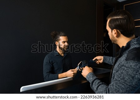 Caucasian man client paying with a credit card for a hair cut or grooming services at the elegant barber shop