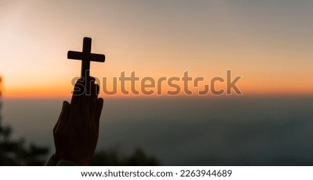 Silhouette of young woman kneeling down praying and holding christian cross for worshipping God at sunset background. concept of christian kneeling and praying to god.