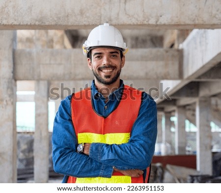 portrait of engineer or worker in safety equipment vest and helmet standing with crossed arms while inspect and discuss the infrastructure of building construction progress at site