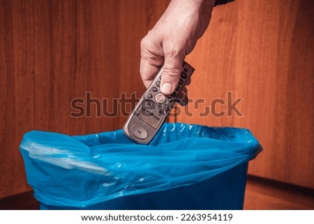 A man throws an old push-button radiotelephone into a trash can. Man's hand with a push-button telephone and a trash can in blue. Royalty-Free Stock Photo #2263954119