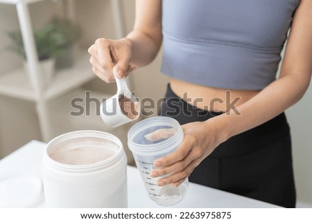 Diet meal replacement for weight loss, asian young woman in sportswear, hand in holding scoop making protein into bottle to shake, drink supplement for muscle after workout at home. Healthy body care. Royalty-Free Stock Photo #2263975875
