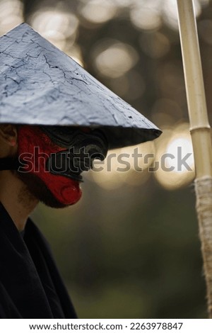 Surrealism theme: a man in a hannya mask, black kimono, black hat with a bamboo stick in his hands in the forest. Surreal image of a man in a hannya half mask, kimono. Surreal samurai, surreal ninja Royalty-Free Stock Photo #2263978847