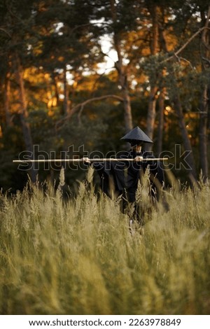 Surrealism theme: a man in a hannya mask, black kimono, black hat with a bamboo stick in his hands in the forest. Surreal image of a man in a hannya half mask, kimono. Surreal samurai, surreal ninja Royalty-Free Stock Photo #2263978849