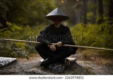 Surrealism theme: a man in a hannya mask, black kimono, black hat with a bamboo stick in his hands in the forest. Surreal image of a man in a hannya half mask, kimono. Surreal samurai, surreal ninja Royalty-Free Stock Photo #2263978851