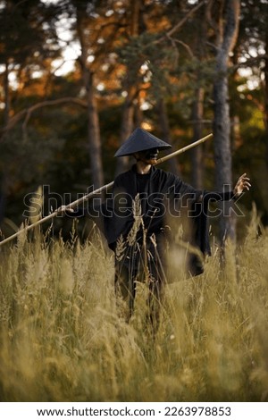 Surrealism theme: a man in a hannya mask, black kimono, black hat with a bamboo stick in his hands in the forest. Surreal image of a man in a hannya half mask, kimono. Surreal samurai, surreal ninja Royalty-Free Stock Photo #2263978853