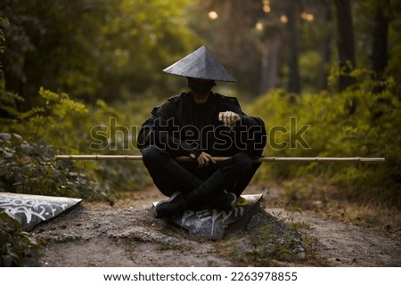 Surrealism theme: a man in a hannya mask, black kimono, black hat with a bamboo stick in his hands in the forest. Surreal image of a man in a hannya half mask, kimono. Surreal samurai, surreal ninja Royalty-Free Stock Photo #2263978855