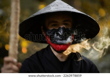 Surrealism theme: a man in a hannya mask, black kimono, black hat with a bamboo stick in his hands in the forest. Surreal image of a man in a hannya half mask, kimono. Surreal samurai, surreal ninja Royalty-Free Stock Photo #2263978859