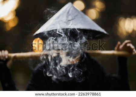 Surrealism theme: a man in a hannya mask, black kimono, black hat with a bamboo stick in his hands in the forest. Surreal image of a man in a hannya half mask, kimono. Surreal samurai, surreal ninja Royalty-Free Stock Photo #2263978861