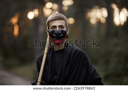 Surrealism theme: a man in a hannya mask, black kimono, black hat with a bamboo stick in his hands in the forest. Surreal image of a man in a hannya half mask, kimono. Surreal samurai, surreal ninja Royalty-Free Stock Photo #2263978863