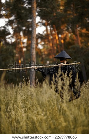 Surrealism theme: a man in a hannya mask, black kimono, black hat with a bamboo stick in his hands in the forest. Surreal image of a man in a hannya half mask, kimono. Surreal samurai, surreal ninja Royalty-Free Stock Photo #2263978865