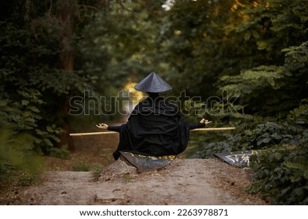 Surrealism theme: a man in a hannya mask, black kimono, black hat with a bamboo stick in his hands in the forest. Surreal image of a man in a hannya half mask, kimono. Surreal samurai, surreal ninja Royalty-Free Stock Photo #2263978871