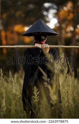 Surrealism theme: a man in a hannya mask, black kimono, black hat with a bamboo stick in his hands in the forest. Surreal image of a man in a hannya half mask, kimono. Surreal samurai, surreal ninja Royalty-Free Stock Photo #2263978875