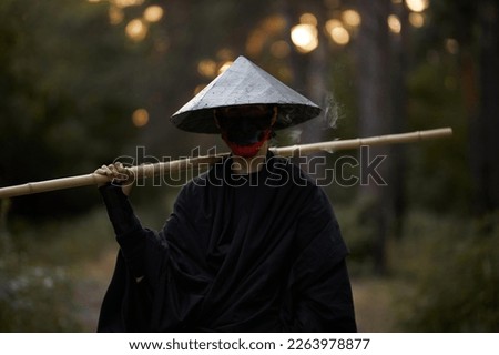 Surrealism theme: a man in a hannya mask, black kimono, black hat with a bamboo stick in his hands in the forest. Surreal image of a man in a hannya half mask, kimono. Surreal samurai, surreal ninja Royalty-Free Stock Photo #2263978877
