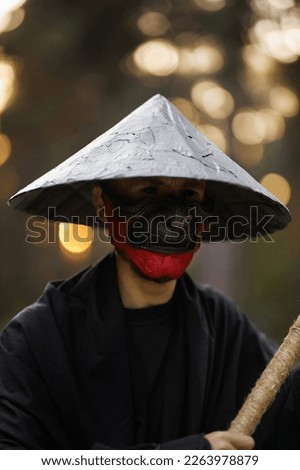 Surrealism theme: a man in a hannya mask, black kimono, black hat with a bamboo stick in his hands in the forest. Surreal image of a man in a hannya half mask, kimono. Surreal samurai, surreal ninja Royalty-Free Stock Photo #2263978879