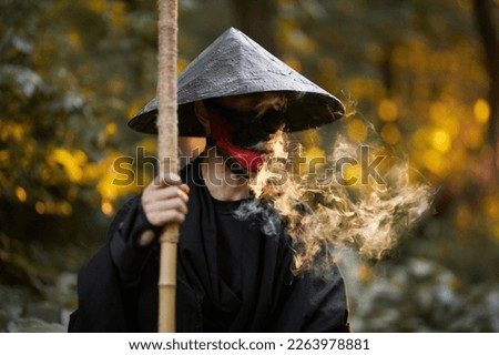 Surrealism theme: a man in a hannya mask, black kimono, black hat with a bamboo stick in his hands in the forest. Surreal image of a man in a hannya half mask, kimono. Surreal samurai, surreal ninja Royalty-Free Stock Photo #2263978881