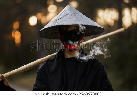 Surrealism theme: a man in a hannya mask, black kimono, black hat with a bamboo stick in his hands in the forest. Surreal image of a man in a hannya half mask, kimono. Surreal samurai, surreal ninja Royalty-Free Stock Photo #2263978883