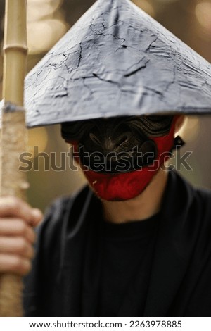 Surrealism theme: a man in a hannya mask, black kimono, black hat with a bamboo stick in his hands in the forest. Surreal image of a man in a hannya half mask, kimono. Surreal samurai, surreal ninja Royalty-Free Stock Photo #2263978885