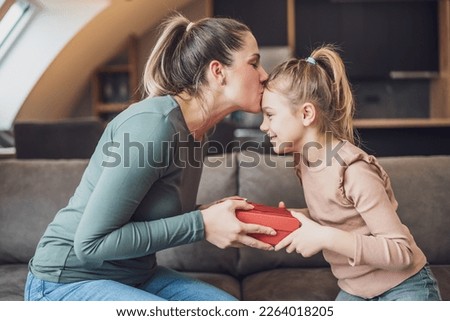 Happy mother is kissing her daughter while  getting gift from her.