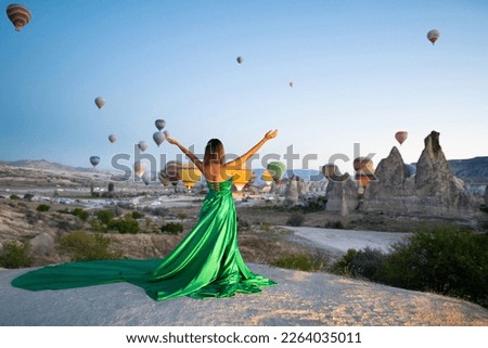 a girl in a flying dress with a long train on the background of balloons in Cappadocia