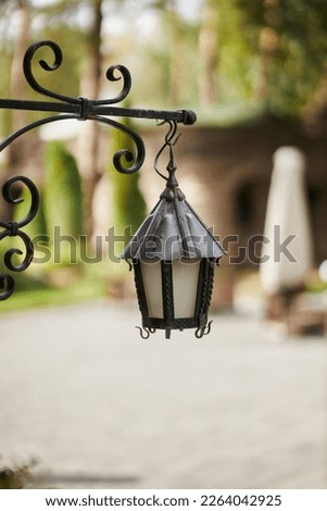 vintage street metal lamp on blurred background. iron lantern against the wall. A vintage metal lamp attached to the wall of a building. Close up photo of vintage street light mounted on a wall. Royalty-Free Stock Photo #2264042925